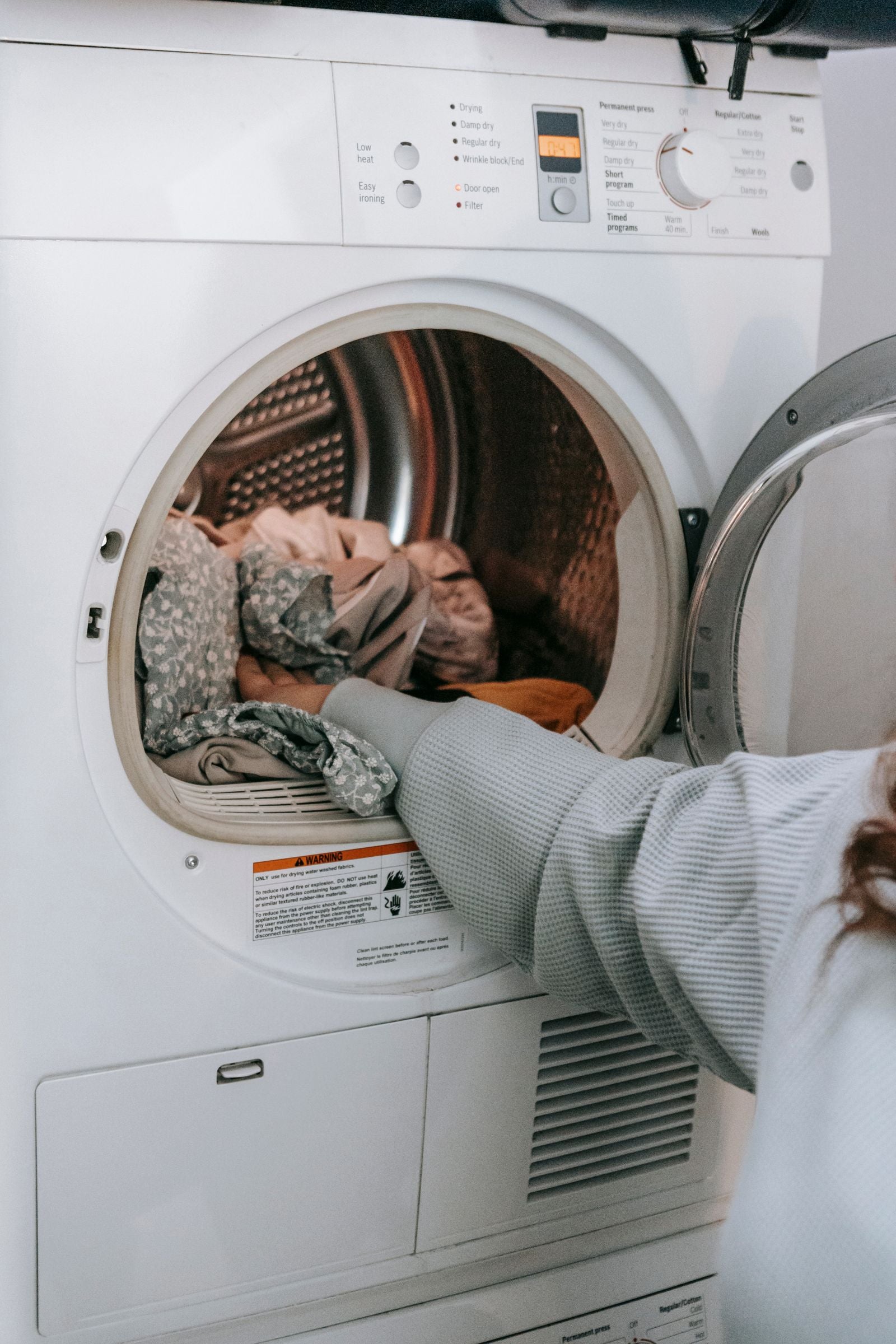 Modern front load laundry machine with hands loading clothes for dryer vent maintenance